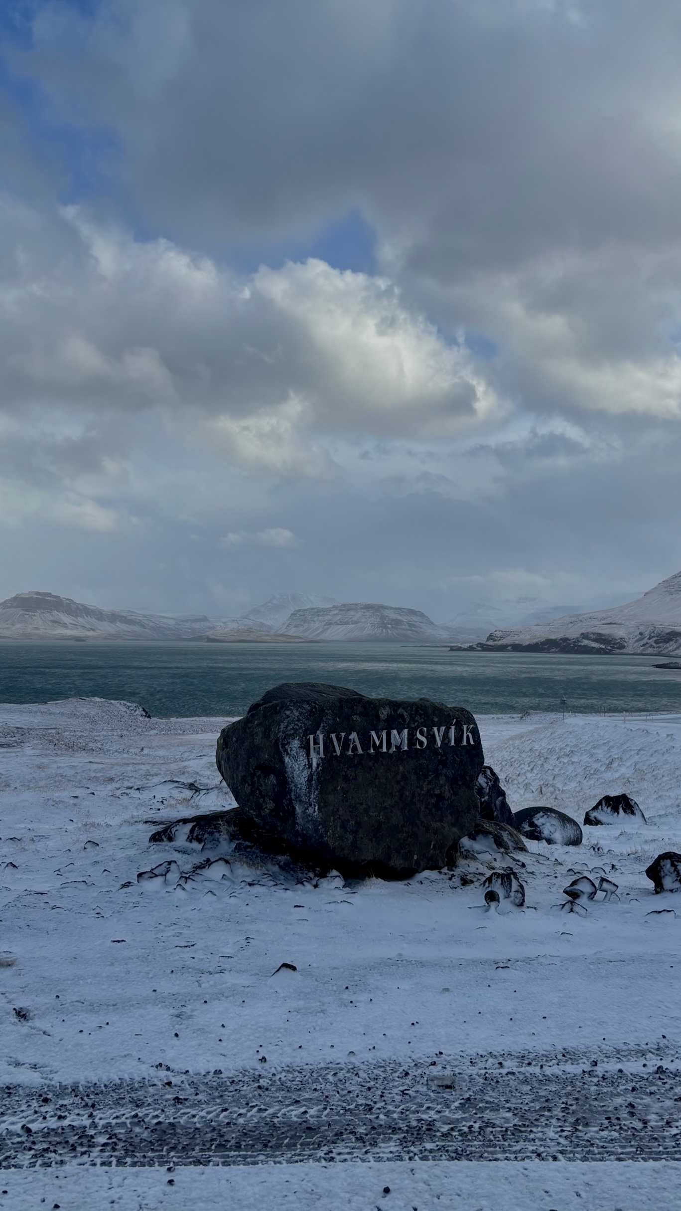 Engraved rock sitting in snow with the ocean and mountains in the background.