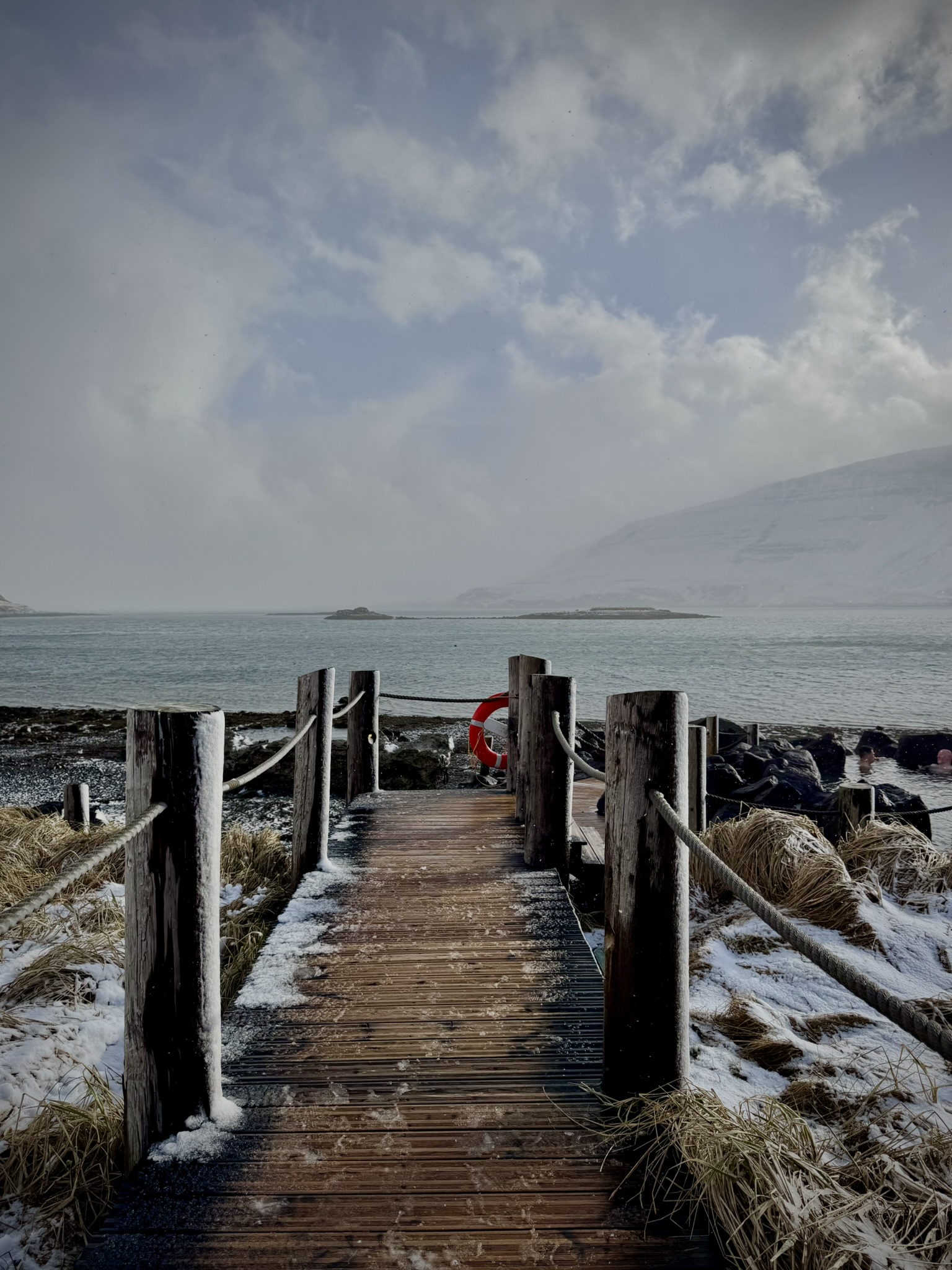 Winter ocean view from a wooden deck and a mountain in the background.